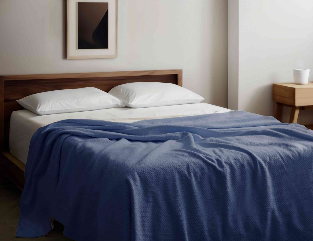 Organic Cotton Blanket in blue draped over a modern wooden bed, GOTS certified and hypoallergenic, ideal for year-round comfort and style.