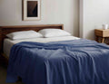 Organic Cotton Blanket in blue draped over a modern wooden bed, GOTS certified and hypoallergenic, ideal for year-round comfort and style.