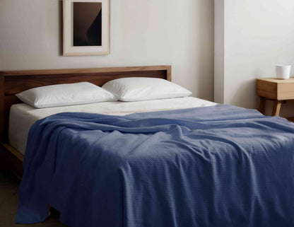 Organic Cotton Blanket in blue draped over a modern wooden bed, GOTS certified and hypoallergenic, ideal for year-round comfort and style.
